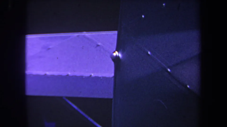 Close-up home-movie frame of the aircraft's wing edge and dark panel, with a small fitting visible under strong purple-blue cast.