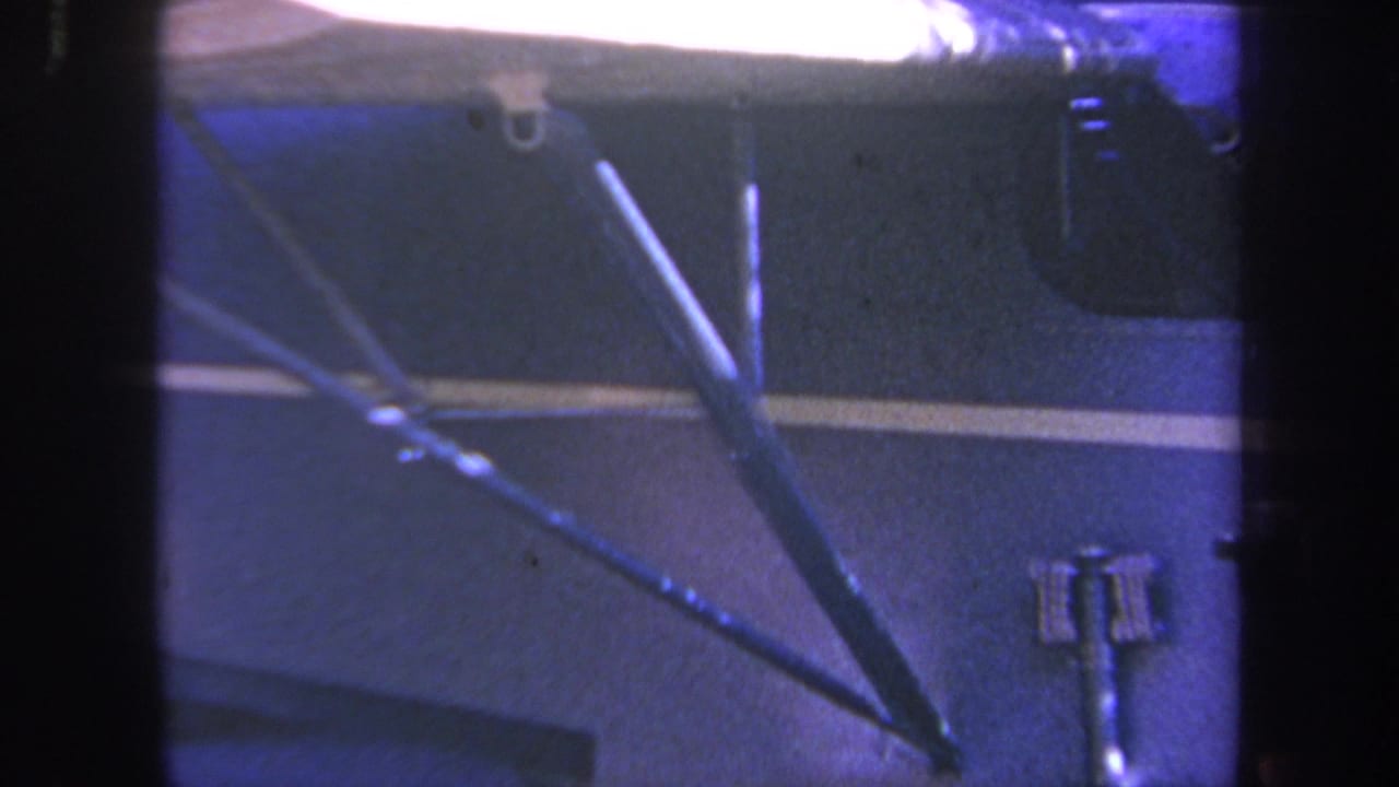 Dark blue vehicle side with white stripe and metal arms in a dim workshop.