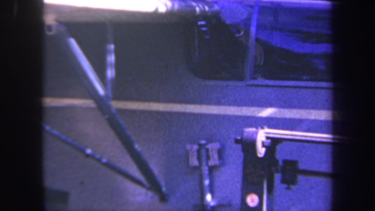 Blue-tinted 8mm frame of a vehicle side panel and mounted workshop fixture, supported by metadata as Volmer Yucaipa, California, 1969.