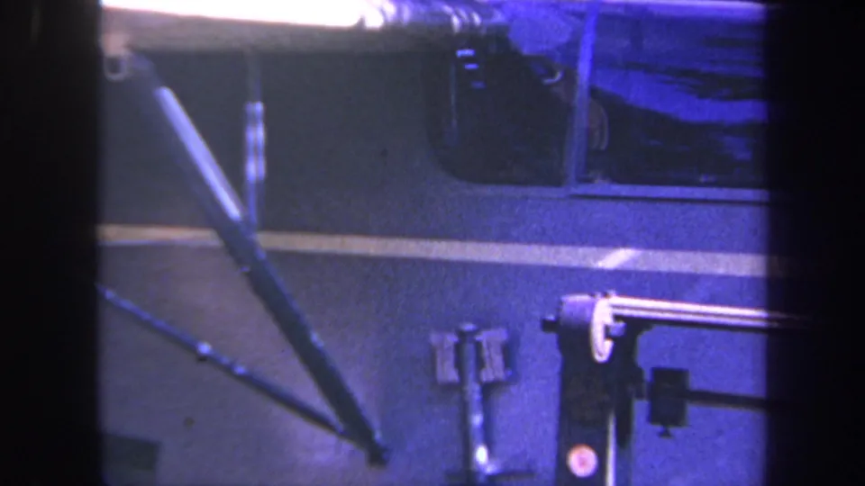 Blue-tinted 8mm frame of a vehicle side panel and mounted workshop fixture, supported by metadata as Volmer Yucaipa, California, 1969.