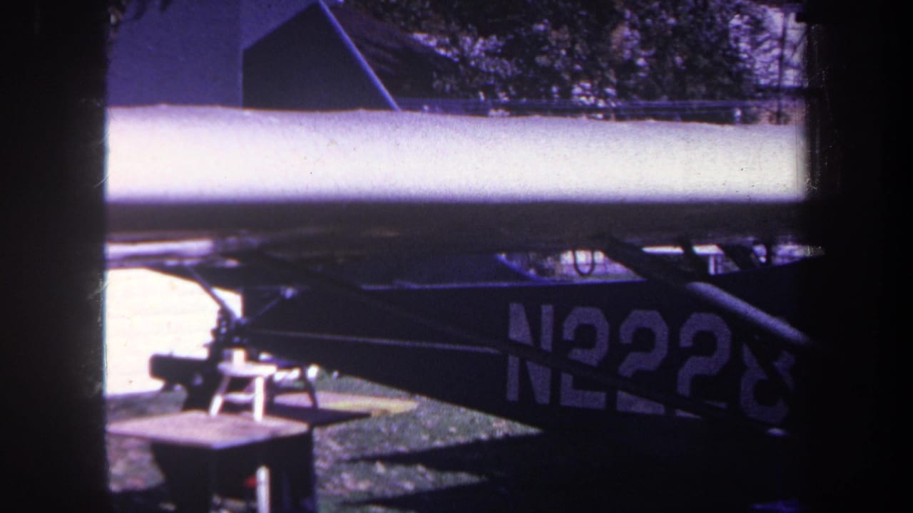 Small aircraft wing and tail section beside a brick wall, with partial N2228 marking visible.