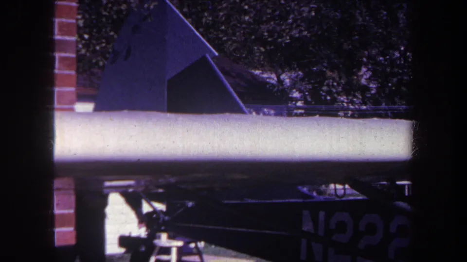 1969 8mm frame from Yucaipa showing the small aircraft's wing and tail area, with a stool below and partial N2228 marking.