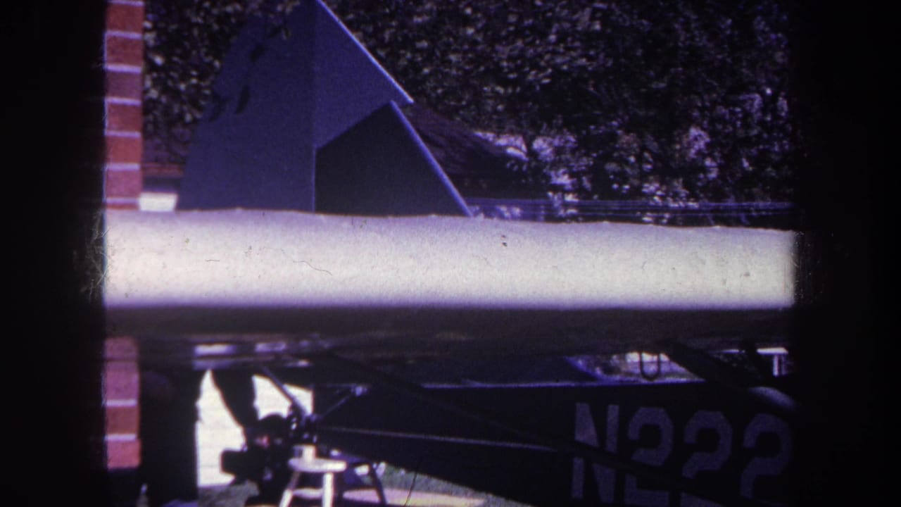 Small aircraft wing and partial N2228 registration seen through a dark frame with brick at left.