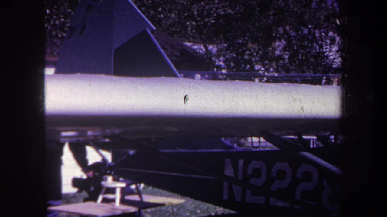 1969 Yucaipa 8mm frame with a small aircraft wing crossing the view, partial N2228 marking, trees, and shadowed framing.