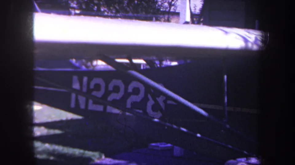 1969 Yucaipa-area 8mm frame showing a close blue aircraft side with partial N2228 registration, struts, and strong purple cast.