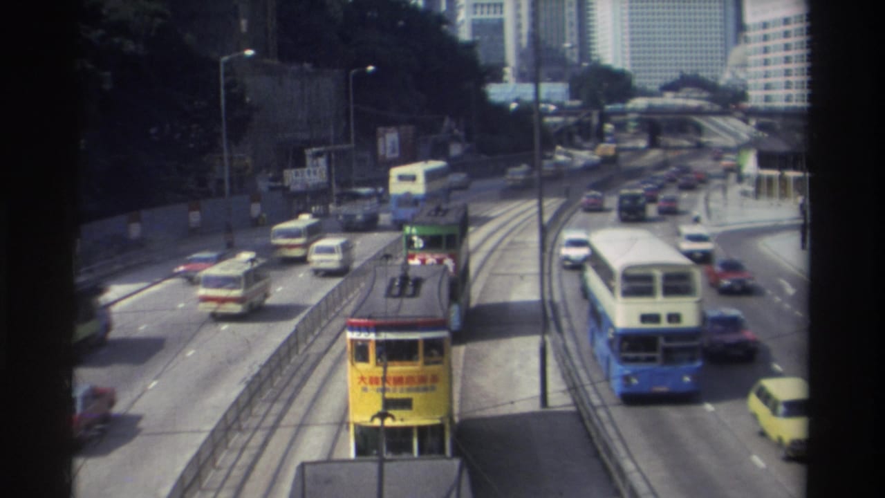 Elevated view of a yellow tram, buses, cars, road signs, and high-rise buildings along a city road.