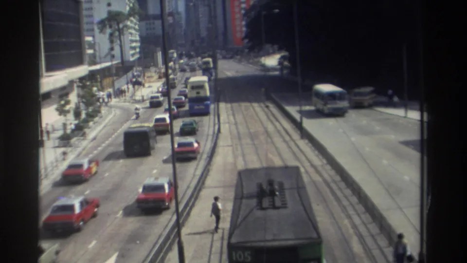 1982 Hong Kong street corridor seen from above, with buses, cars, tram tracks, pedestrians, sidewalks, and high-rise buildings along the road.