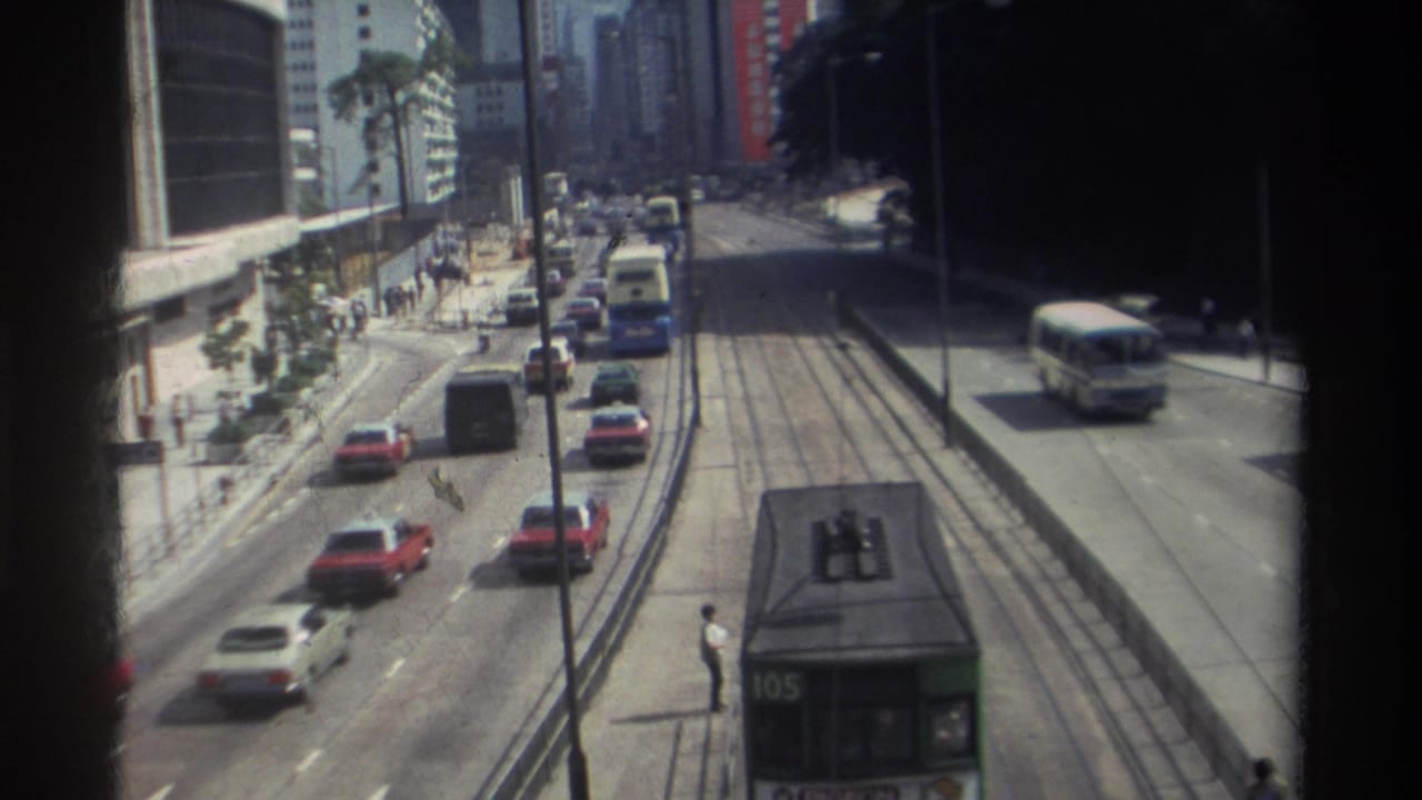 1982 Hong Kong street traffic seen from above, with red and white cars, tram tracks, pedestrians, and a tram partly visible at the bottom.