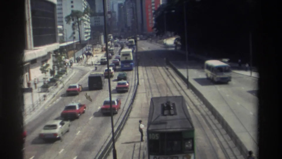 1982 Hong Kong street traffic seen from above, with red and white cars, tram tracks, pedestrians, and a tram partly visible at the bottom.