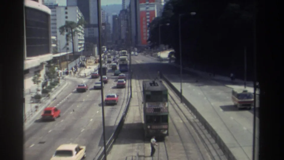 End frame of 1982 Hong Kong street traffic, showing a double-decker tram, red and white cars, a bus, sidewalks, and tall urban buildings.