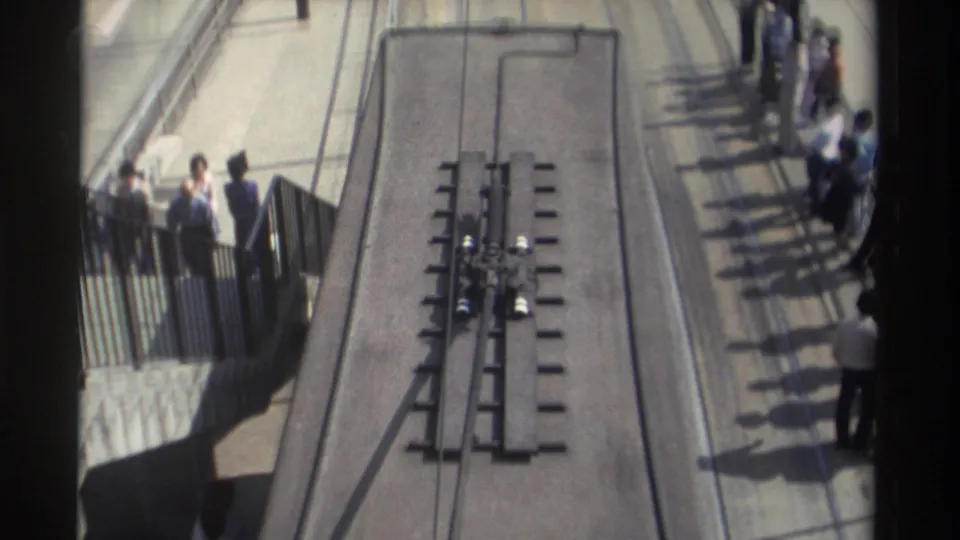 Downward 1982 Hong Kong street view showing tram rails, track hardware, sidewalk railings, and pedestrians gathered near the curb.