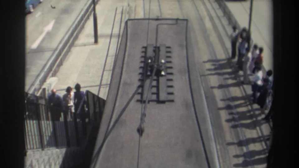 High-angle 1982 Hong Kong street view with tram tracks, a platform of waiting passengers, adjacent traffic lanes, and a dark window frame.