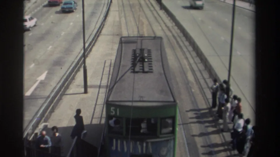 Green double-decker tram number 51 approaches passengers waiting on a 1982 Hong Kong tram platform beside active road traffic.