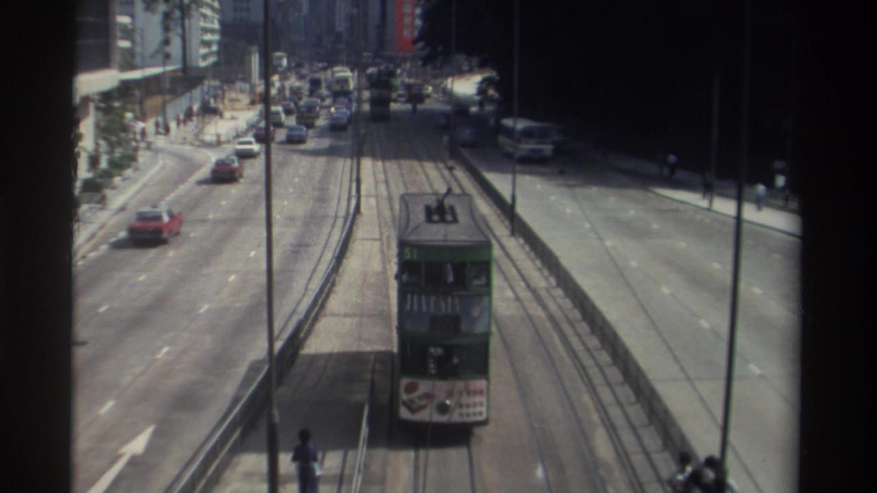 Green double-decker tram approaching along tracks between busy city traffic lanes.