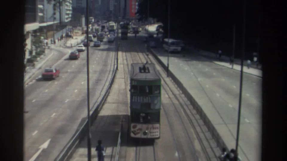 1982 Hong Kong street view with a green double-decker tram, cars, buses, pedestrians, and high-rise buildings seen from above.
