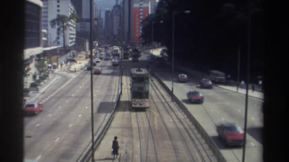1982 Hong Kong street scene from above, with the tram farther down the tracks amid buses, cars, pedestrians, and dense urban buildings.