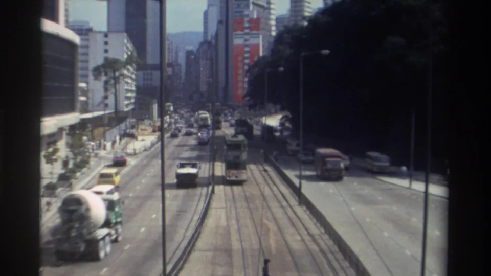1982 Hong Kong traffic view with tram rails, a tram farther up the street, cars, a cement mixer truck, and tall buildings.