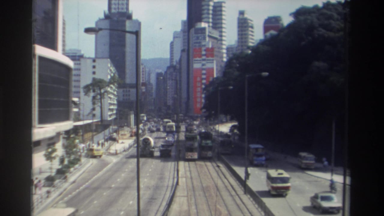 Cars, buses, and a tram corridor run between tall buildings and a wooded roadside slope.