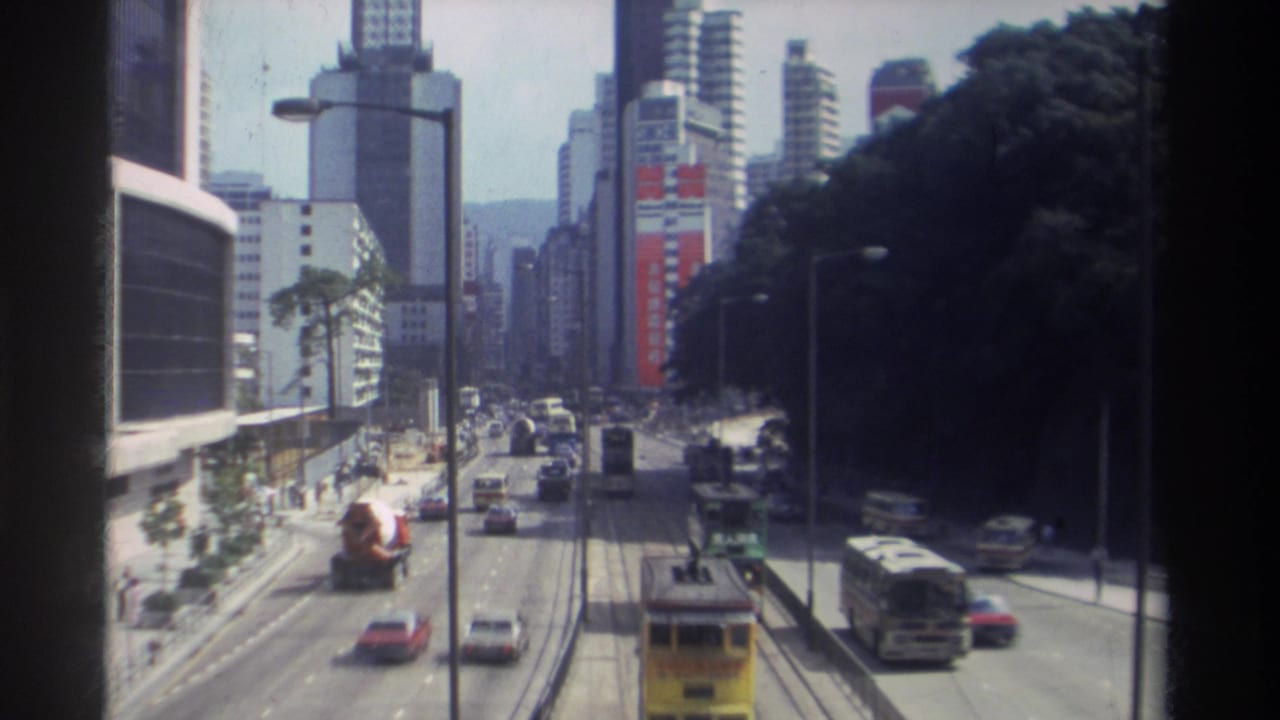 Elevated 1982 Hong Kong street view with mixed traffic, double-decker transit, tall buildings, signage, and a wooded slope at right.
