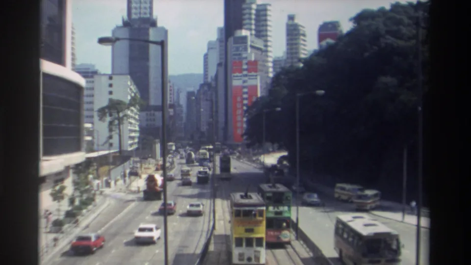 1982 Hong Kong frame from an elevated viewpoint, showing period traffic, double-decker transit, modern towers, and visible commercial signage.