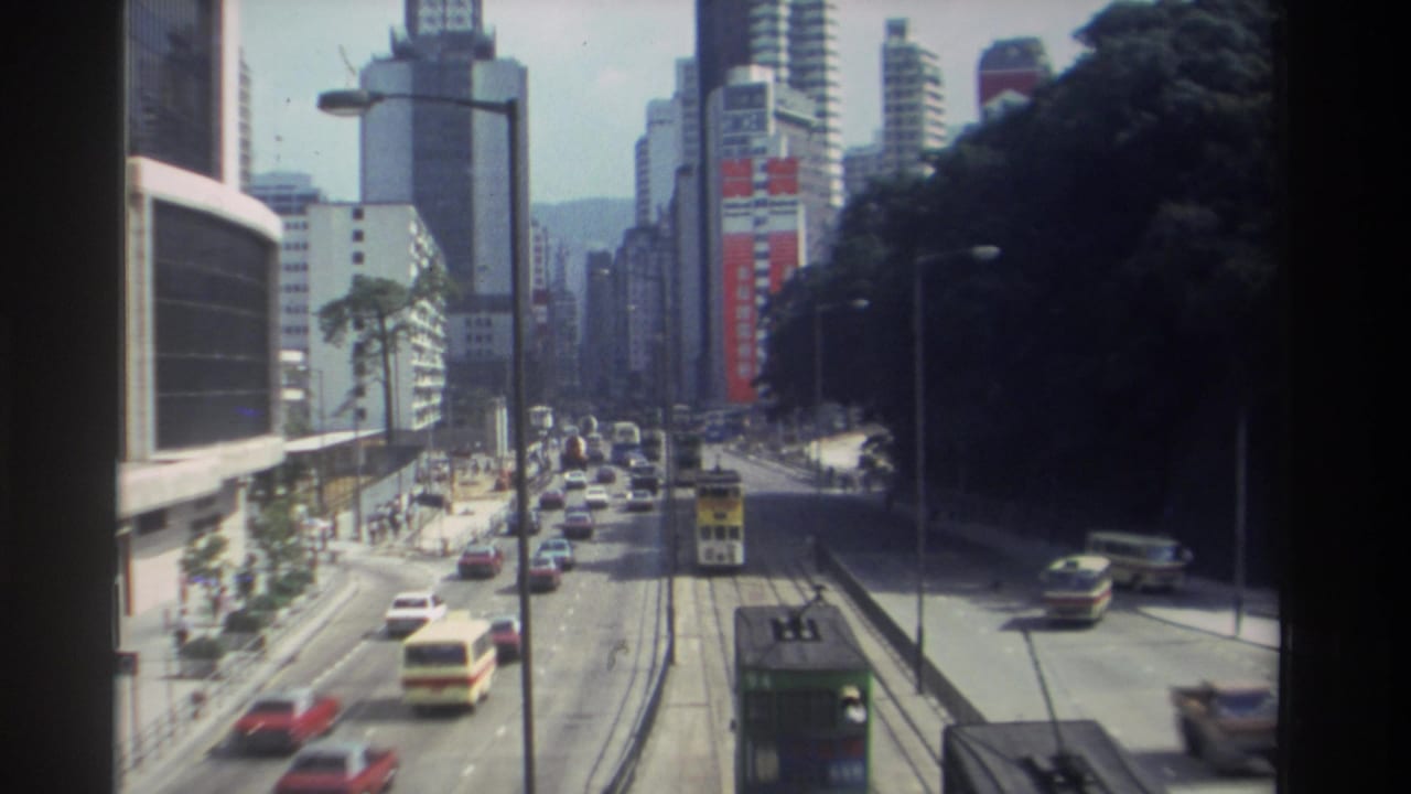 1982 Hong Kong elevated street view showing traffic lanes, tram tracks, double-decker vehicles, hillside greenery, and dense downtown high-rises.