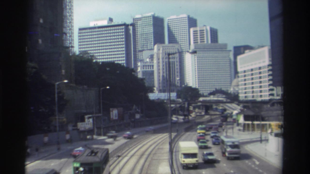 1982 Hong Kong elevated view of tram tracks, buses, mixed car traffic, roadside trees, and office towers across the downtown corridor.