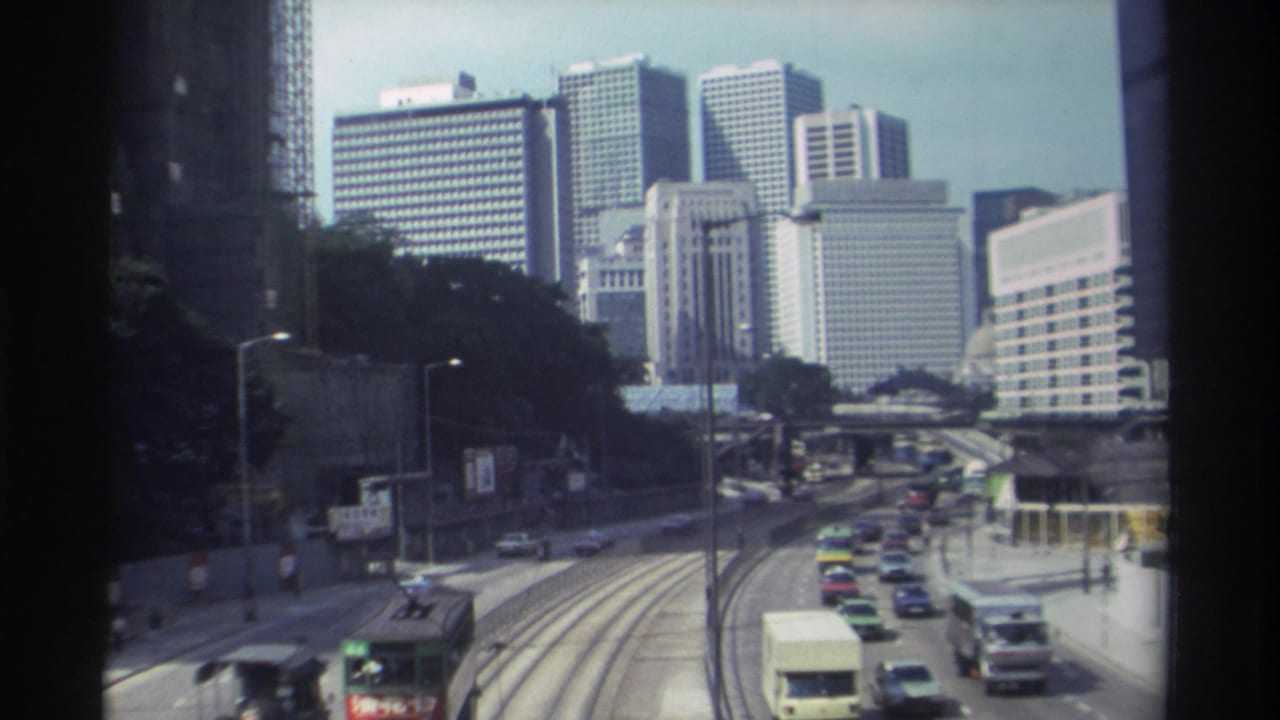1982 Hong Kong home-movie view of cars, a double-decker vehicle, tram tracks, and high-rise buildings from above.