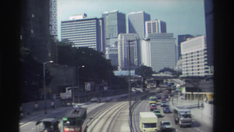 1982 Hong Kong home-movie view of cars, a double-decker vehicle, tram tracks, and high-rise buildings from above.