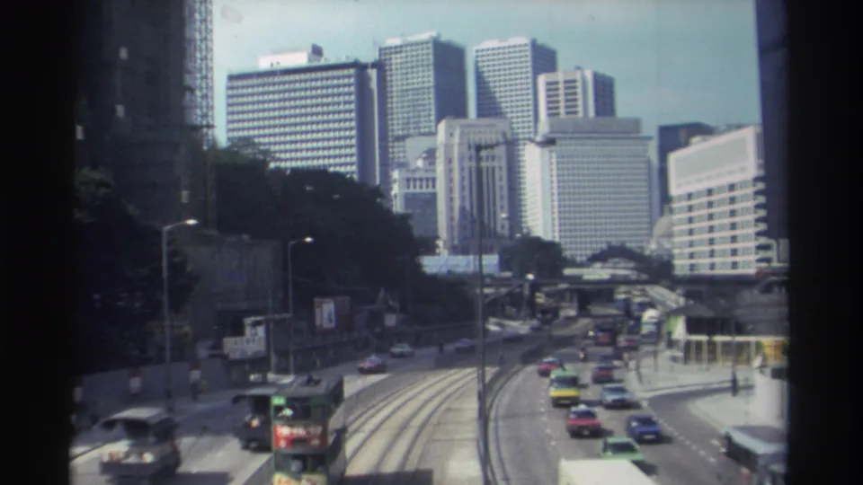 Elevated 1982 Hong Kong street view with cars, a double-decker vehicle, road markings, and modern high-rises.