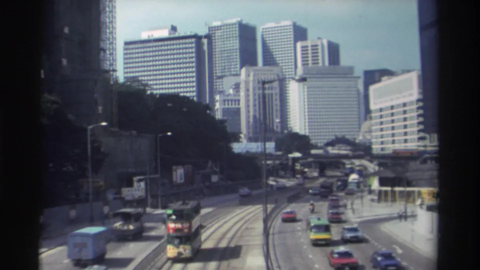 1982 Hong Kong elevated view showing cars, a double-decker tram or bus, delivery vehicles, tracks, and a high-rise skyline.