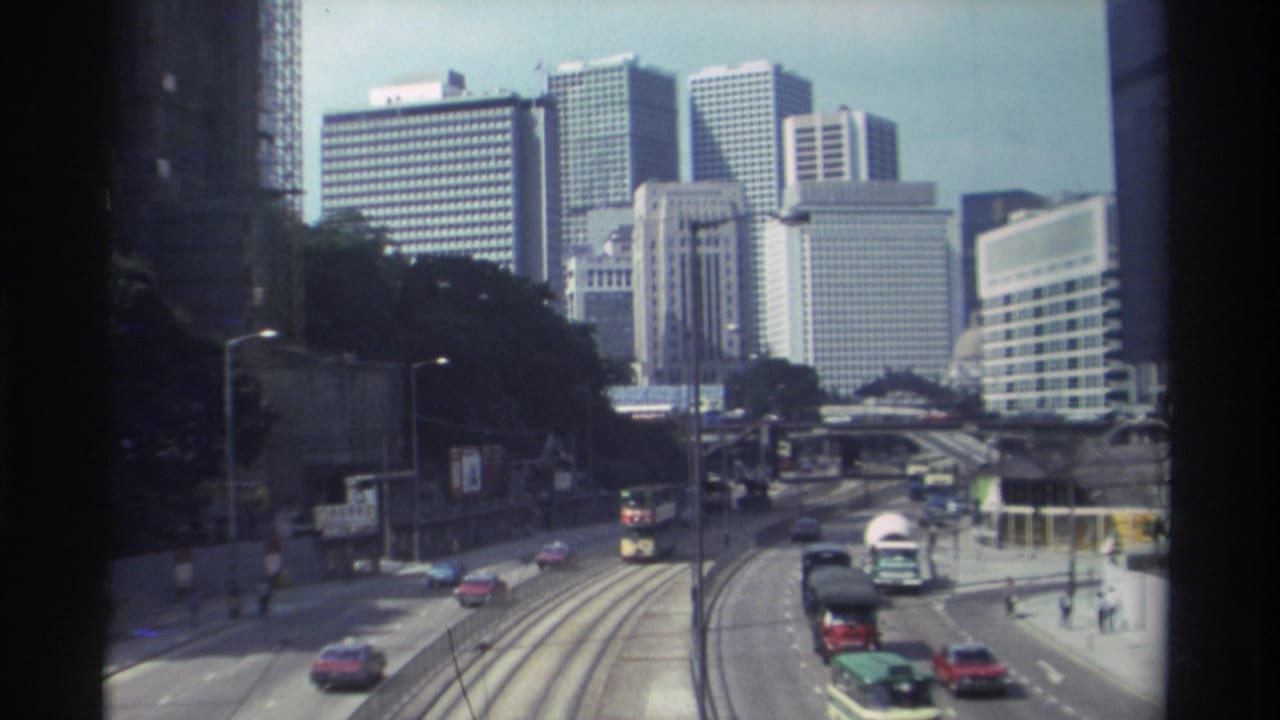 1982 Hong Kong street view from above, showing multi-lane traffic, tram tracks, pedestrians, and a dense skyline of office towers.