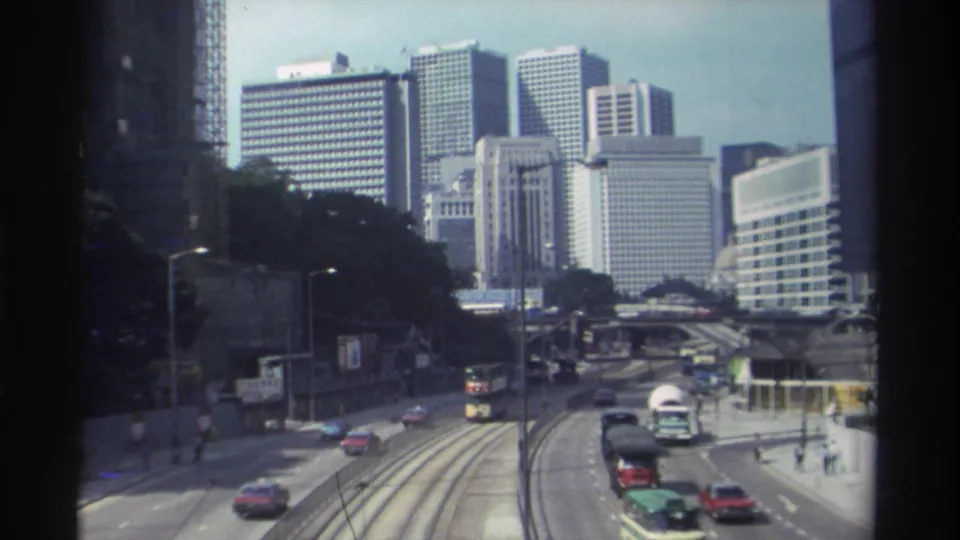 1982 Hong Kong street view from above, showing multi-lane traffic, tram tracks, pedestrians, and a dense skyline of office towers.