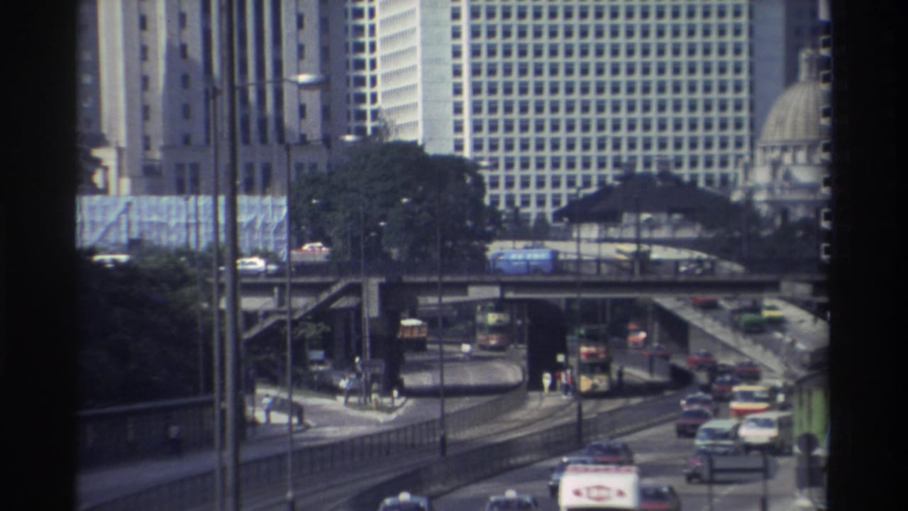 Elevated roadway and city traffic with buses, cars, high-rises, and a distant domed roof.