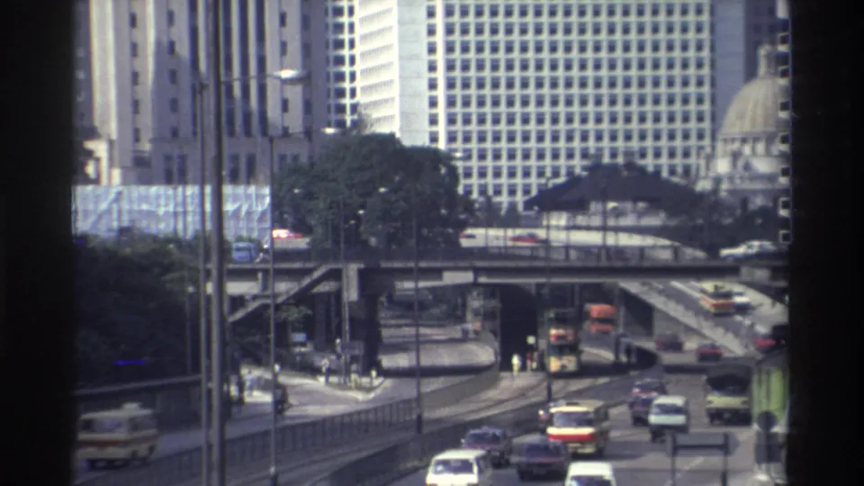 1982 Hong Kong traffic with buses and cars on multi-level roads, seen through a dark vertical window frame.
