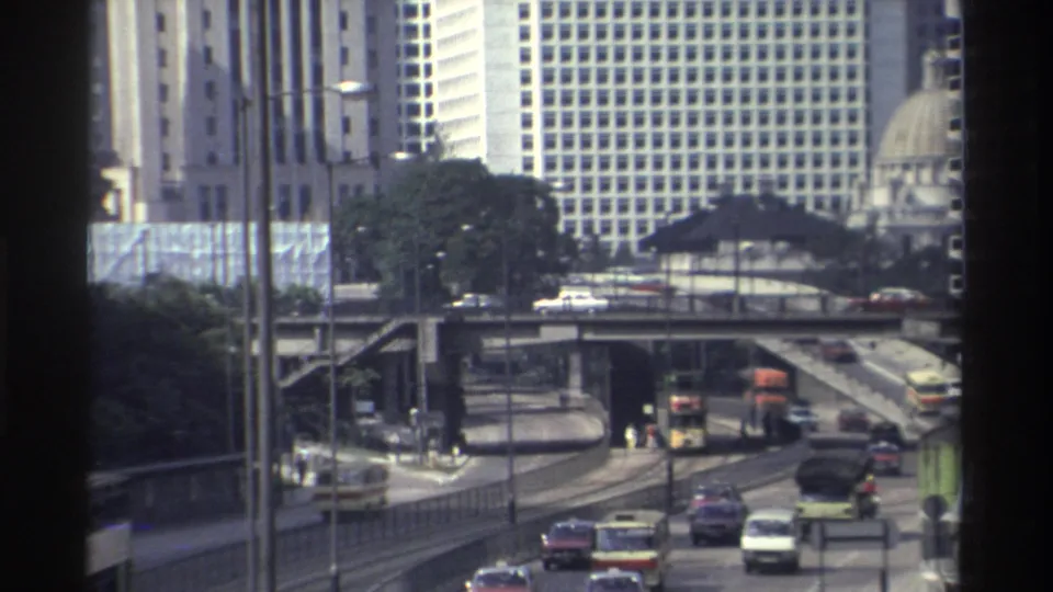 Hong Kong traffic in 1982 passes under and over elevated roads, with older buses and dense office blocks visible.