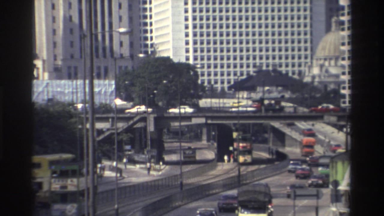 1982 Hong Kong downtown traffic seen through a window frame, with elevated roads, cars, buses, and tall buildings in the background.