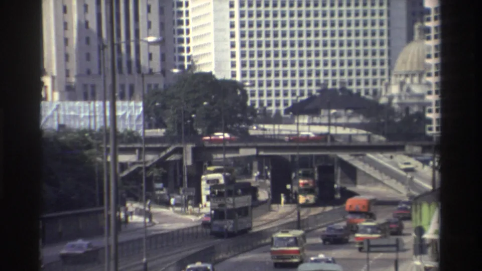 1982 Hong Kong street view showing buses and cars moving through a multi-level roadway below dense modern buildings.