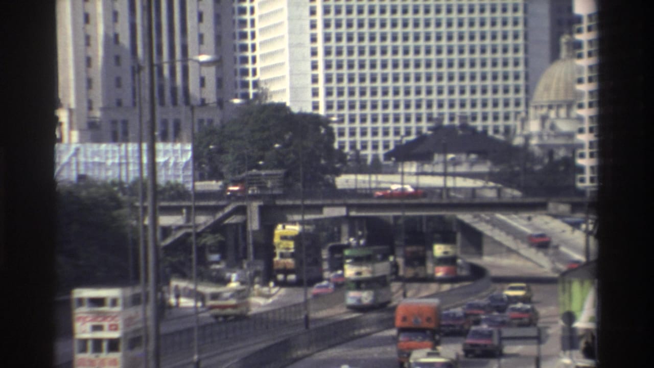 Urban traffic with double-decker buses, cars and trucks passing beneath tall buildings.