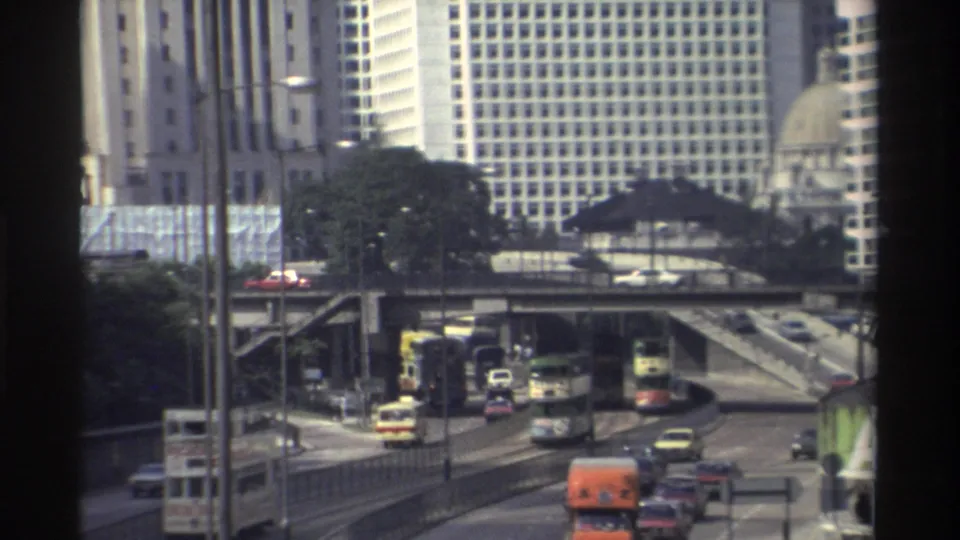 1982 Hong Kong road scene with double-decker buses, cars and trucks moving through elevated streets below tall buildings.