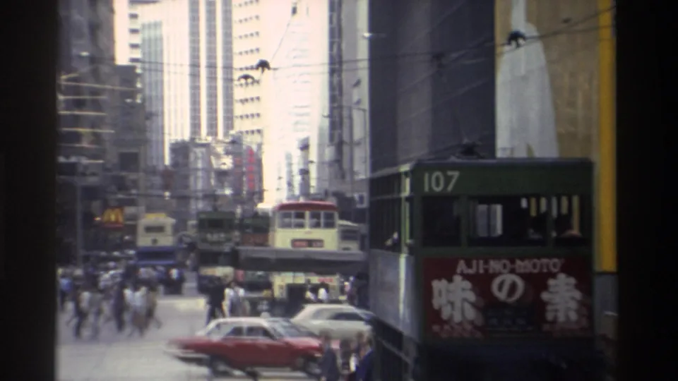 1982 Hong Kong street view with pedestrians crossing among cars and buses, including a close double-decker bus with visible advertising.