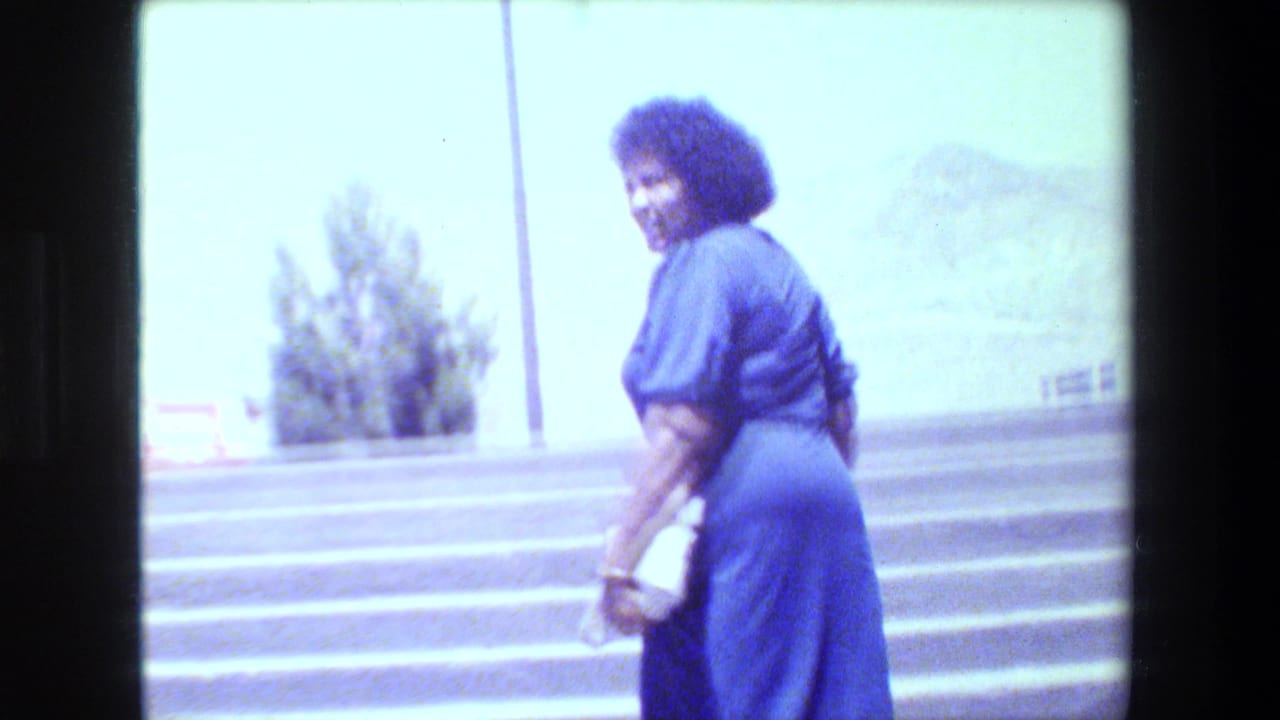 Woman in a blue dress smiles toward the camera while descending outdoor steps, with trees and hazy hills behind her.