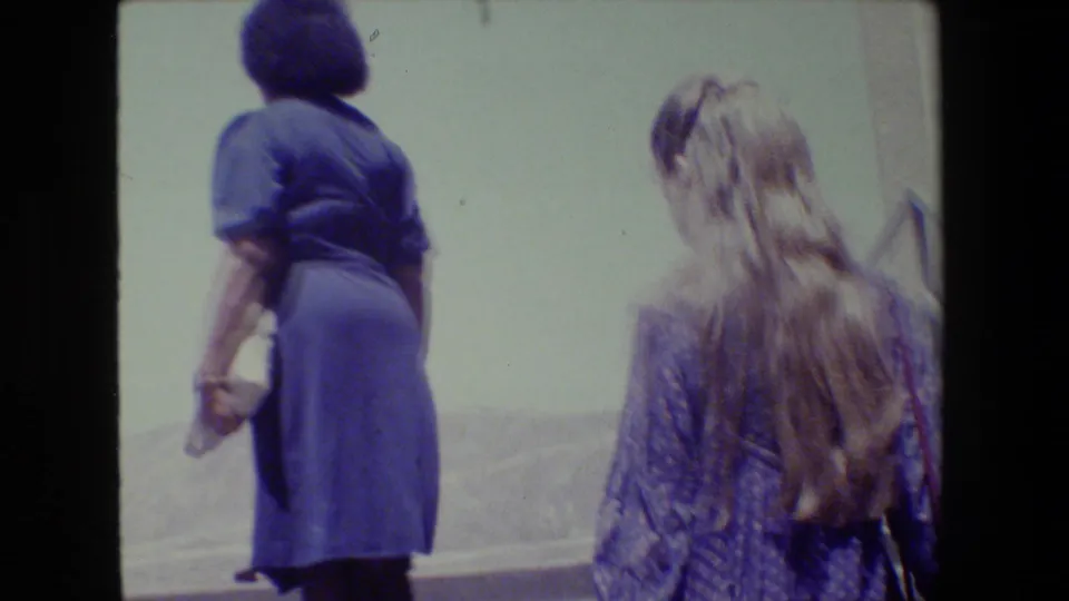 The two women are seen from behind climbing outdoor stairs in supported 1983 Lansing 8mm footage, with hills and railings in the background.