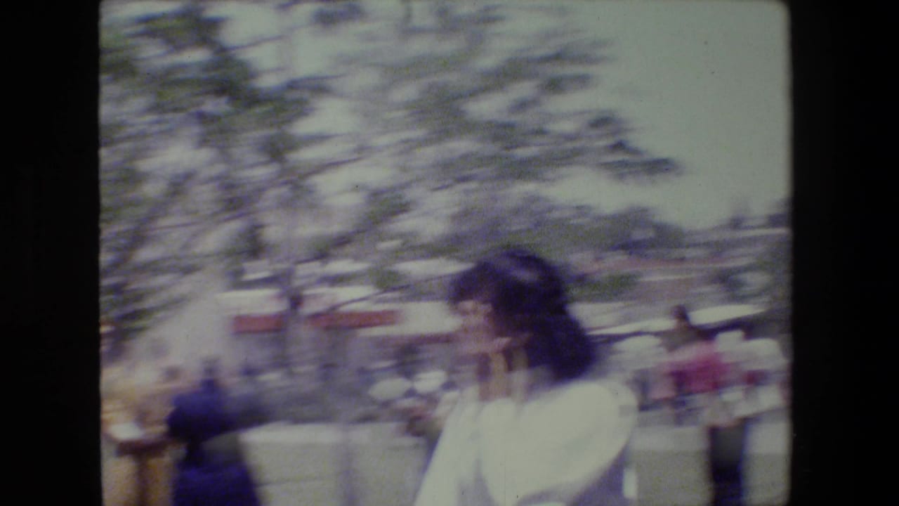 A woman in a light top turns in bright outdoor light during the Lansing, Michigan home-movie gathering.