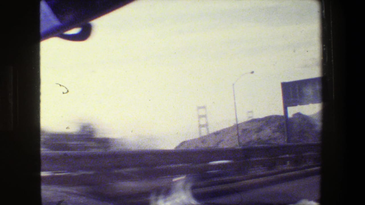 Highway view from inside a moving car with distant bridge towers and hills.