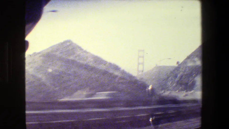 San Francisco 8mm road footage from a moving car, with hills, highway guardrails, blurred traffic, and a distant bridge tower.