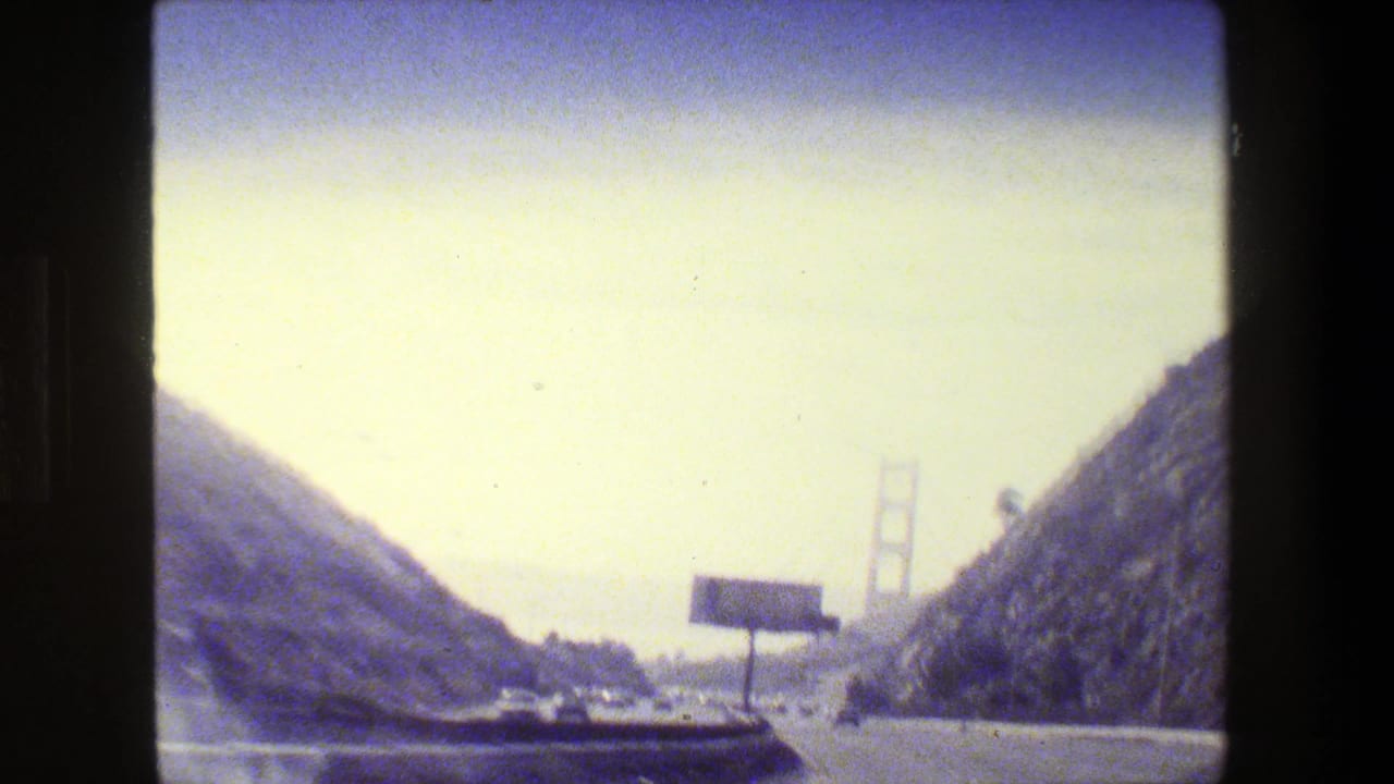 1984 San Francisco home-movie view approaching the Golden Gate Bridge from a multi-lane highway under hazy light.