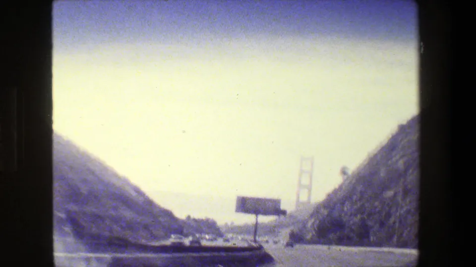 1984 San Francisco home-movie view approaching the Golden Gate Bridge from a multi-lane highway under hazy light.