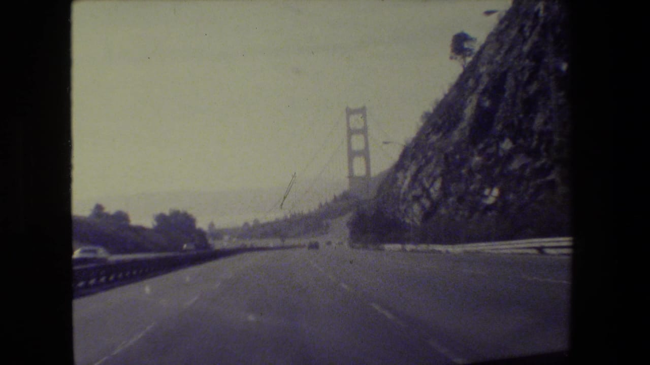 Passenger-view 1984 San Francisco footage showing the roadway leading toward a Golden Gate Bridge tower and hillside.