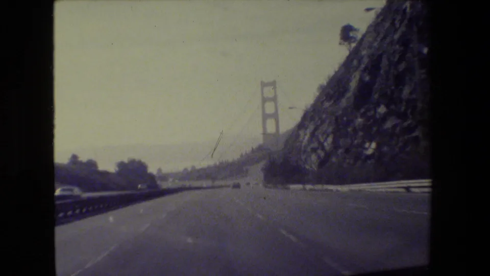 Passenger-view 1984 San Francisco footage showing the roadway leading toward a Golden Gate Bridge tower and hillside.