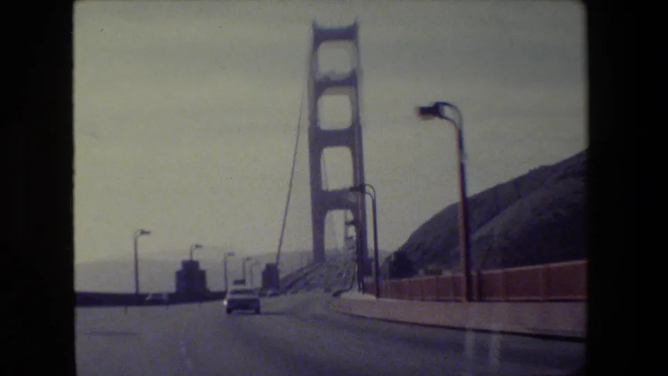 Car-window view on the Golden Gate Bridge in San Francisco, showing the roadway bending toward a tower with vehicles and suspension cables.